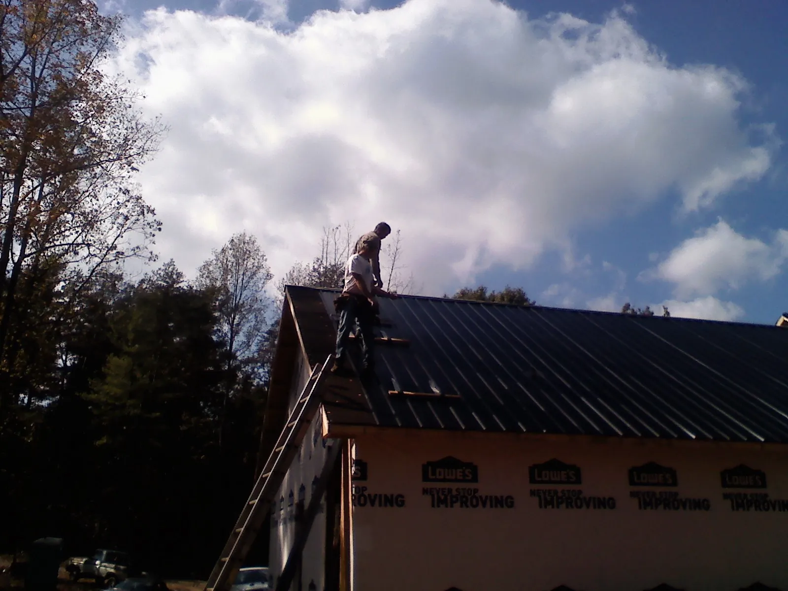 Roofer fastening dark metal panels high against a cloudy sky, from a Roof Inspection job in Blue Ridge